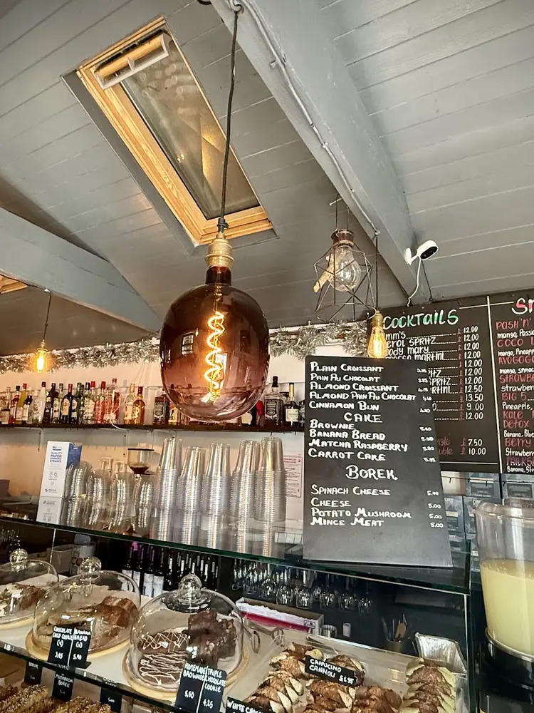 Interior counter with cake domes, hanging filament bulbs and handwritten chalkboard menus for börek, cake and coffee